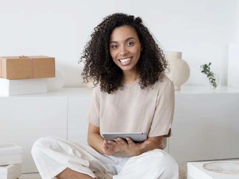 A small-business owner holding a tablet among packages and design materials.
