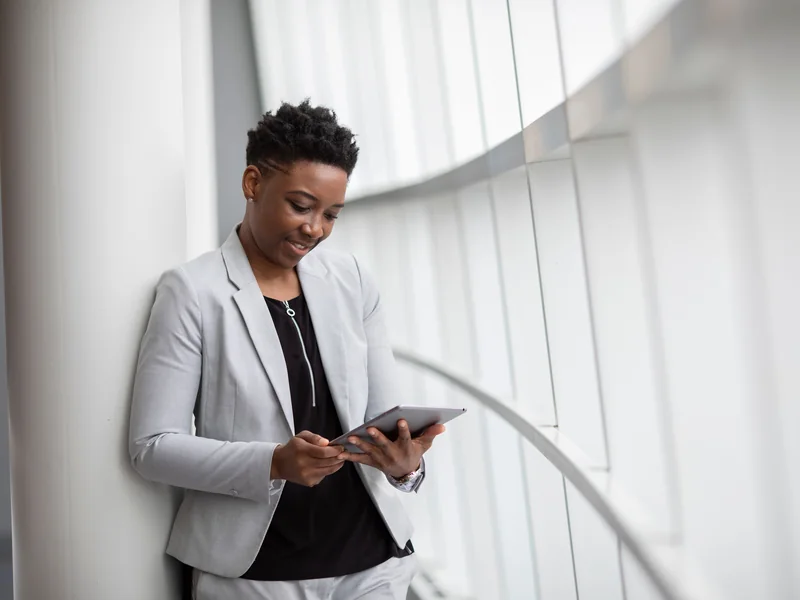 A woman using a tablet beside a bright office window.