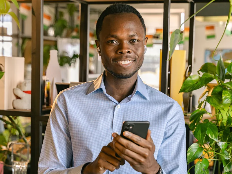 A smiling man holding his smartphone in a bright workspace.